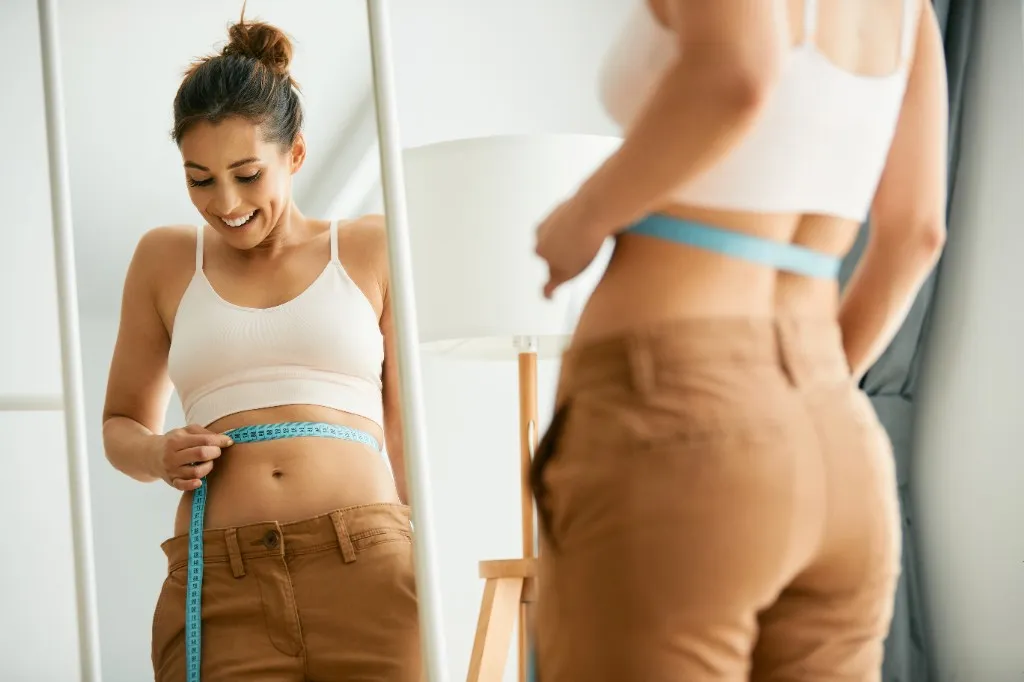 Smiling woman measuring her waist in front of a mirror